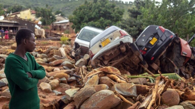 106099428 amanstandsnexttothewreckageavehicleswashedawayfmarch182019inchimanimanieasternzimbabweaftertheareawashitbythecycloneidai.