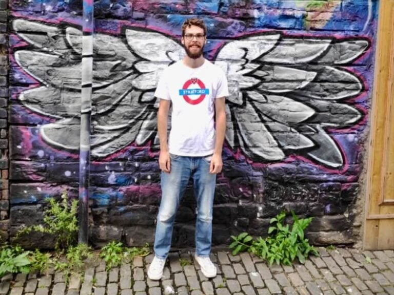 A man standing in front of a mural of angel wings.