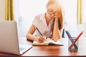 young woman taking note and using laptop while studying at home