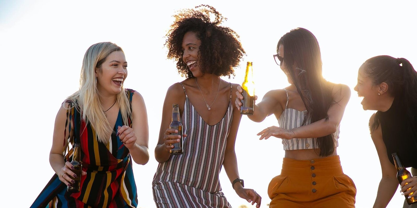 laughing young diverse girlfriends dancing and drinking beer during event